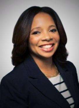 Smiling woman in a professional headshot wearing a navy blazer, standing in front of a light gray background