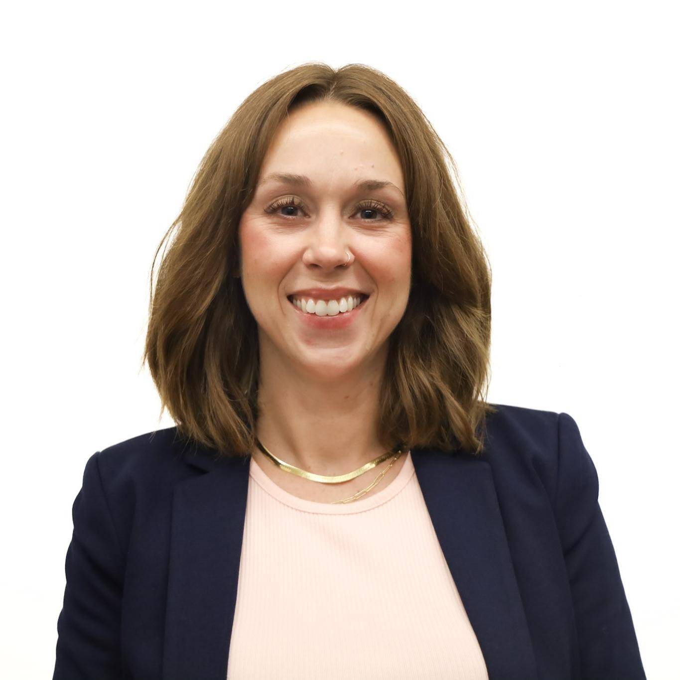 A white woman with shoulder length dark red hair wearing a blue jacket and pink shirt.